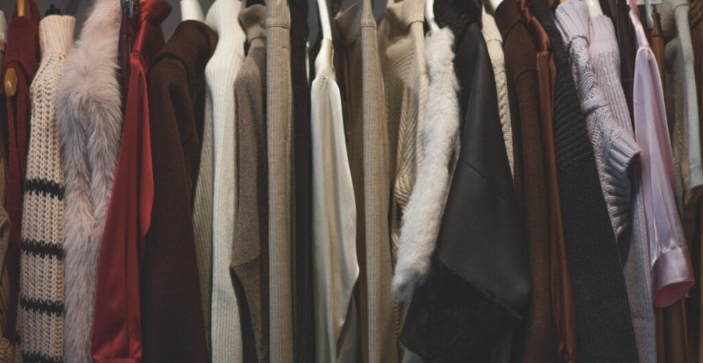 "Cozy closet with a variety of coats and jackets hanging on a rack, featuring textures like fur, wool, and knitwear."

