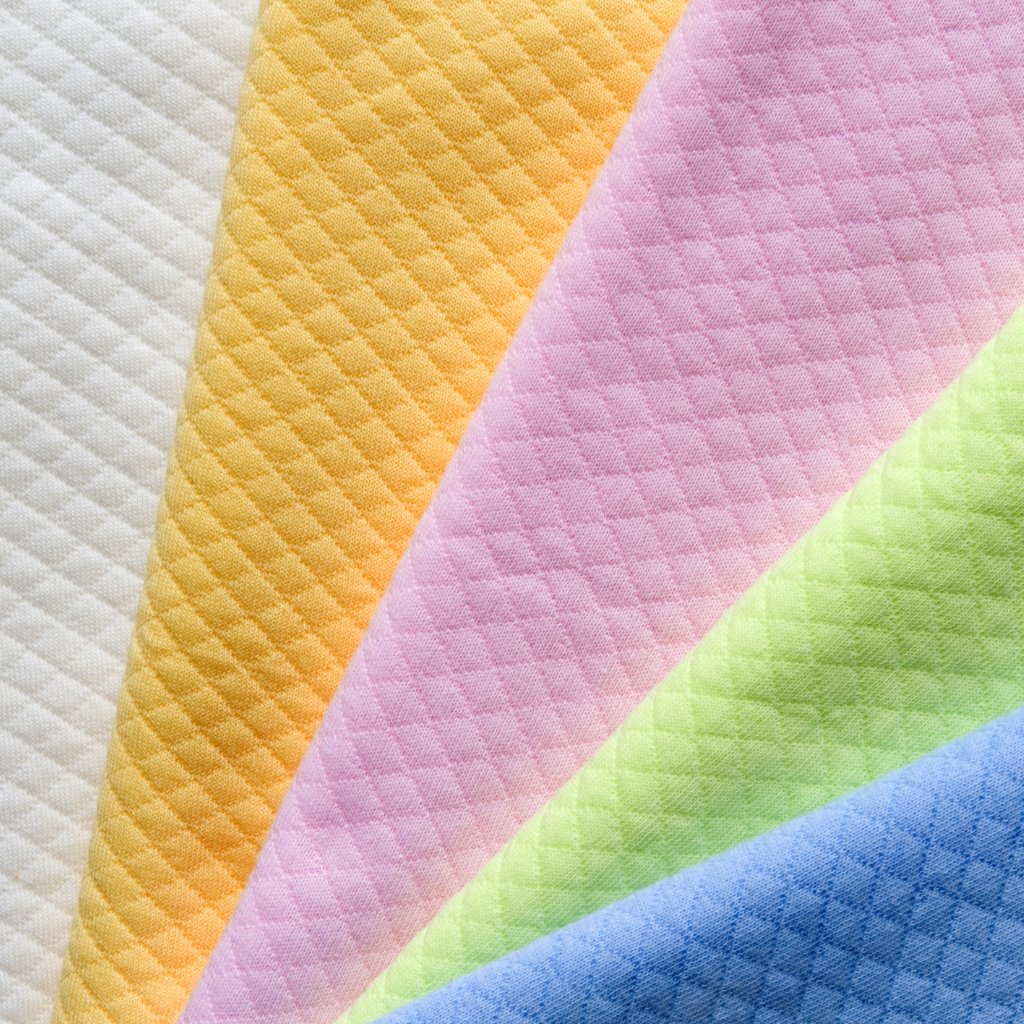 Close-up of quilted velour wool fabric in pastel color blocks: white, orange, pink, lime, and blue with diamond quilting.