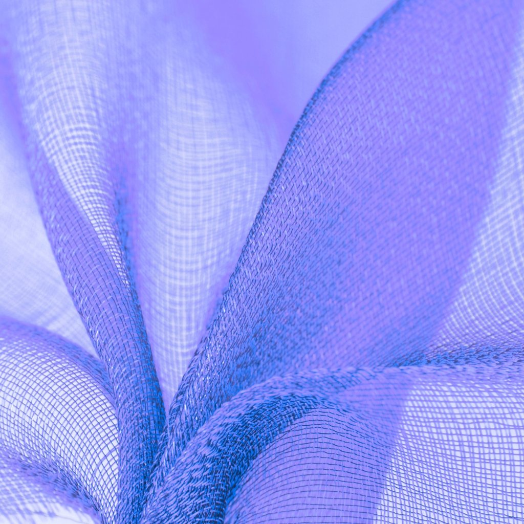 A close-up view of shot organza fabric in varying lavender and blue hues, showing delicate, sheer, and organza-weave texture with soft folds and a subtle sheen.

