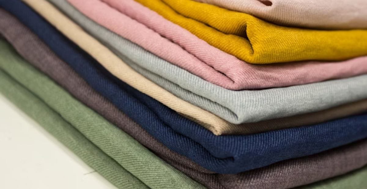 Stack of folded colorful polyester fabrics in different shades including mustard, pink, green, blue, and grey.