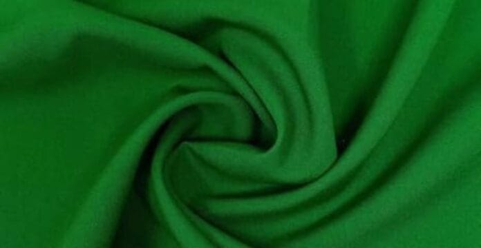 Green polyester fabric folded in swirls, raising the question does polyester make you sweat during wear.is polyester stretchy