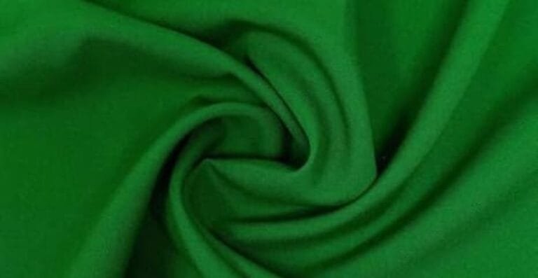Green polyester fabric folded in swirls, raising the question does polyester make you sweat during wear.