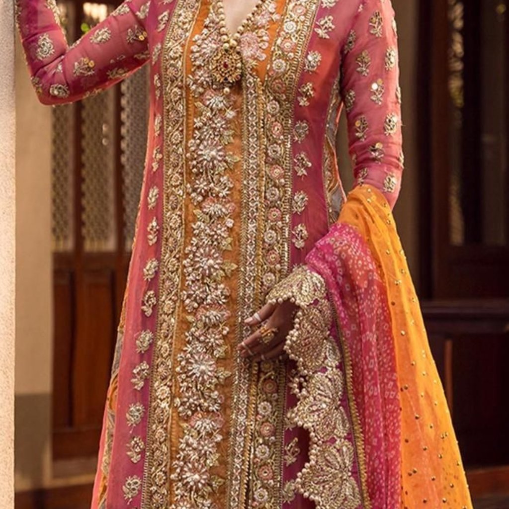 A close-up of a traditional South Asian bridal ensemble featuring a pink and orange heavily embroidered kameez with gold threadwork and beading, paired with an orange dupatta; the wearer’s intricately embellished hand jewelry rests near the midsection.

A close-up of a traditional South Asian bridal ensemble featuring a pink and orange heavily embroidered kameez with gold threadwork and beading, paired with an orange dupatta; the wearer’s intricately embellished hand jewelry rests near the midsection.

