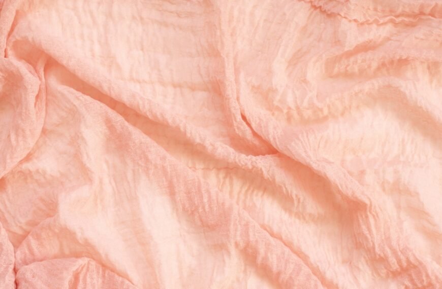 A close-up view of soft, ruffled pink fabric with folds and gentle texture.