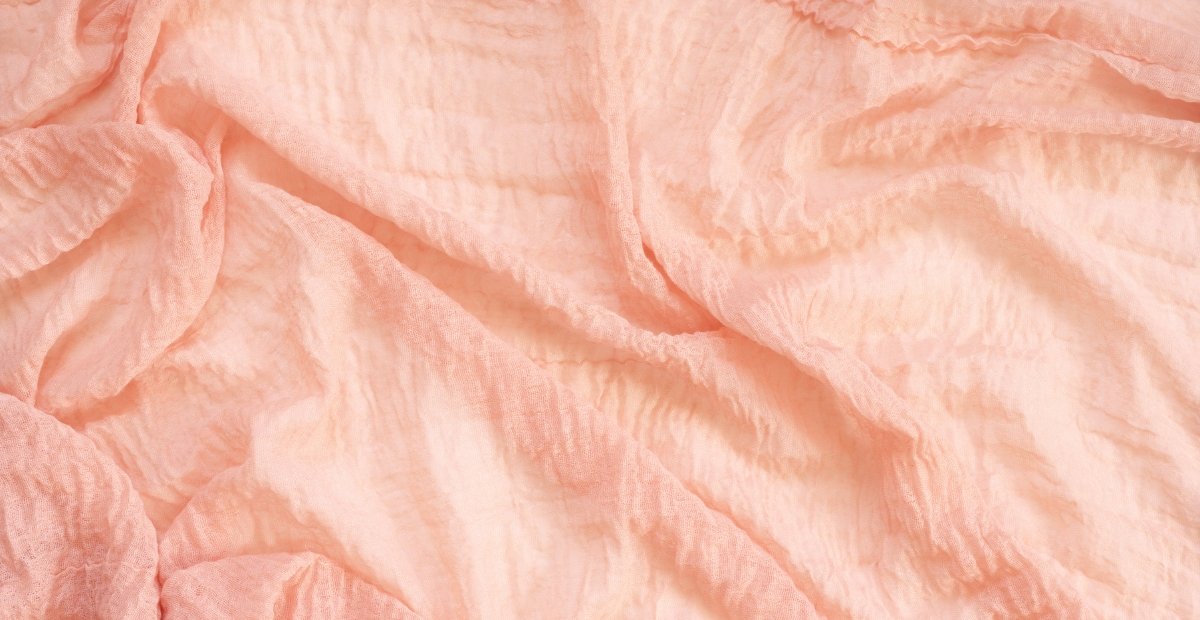 Voile Cotton Fabric: Soft, Durable, and Versatile A close-up view of soft, ruffled pink fabric with folds and gentle texture.