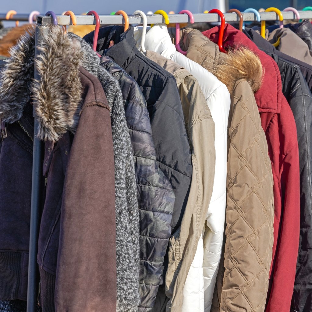 A row of warm winter jackets on a clothing rack, featuring various colors and textures including fur-lined hoods and quilted patterns.If you want a more generic alt text: “Row of jackets on a rack, showcasing different fabrics and colors