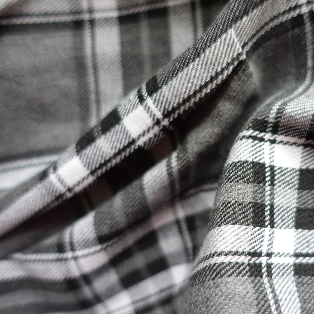 Close-up of plaid flannel fabric in black, white, and gray tones, showing soft, brushed texture and stitched seams.