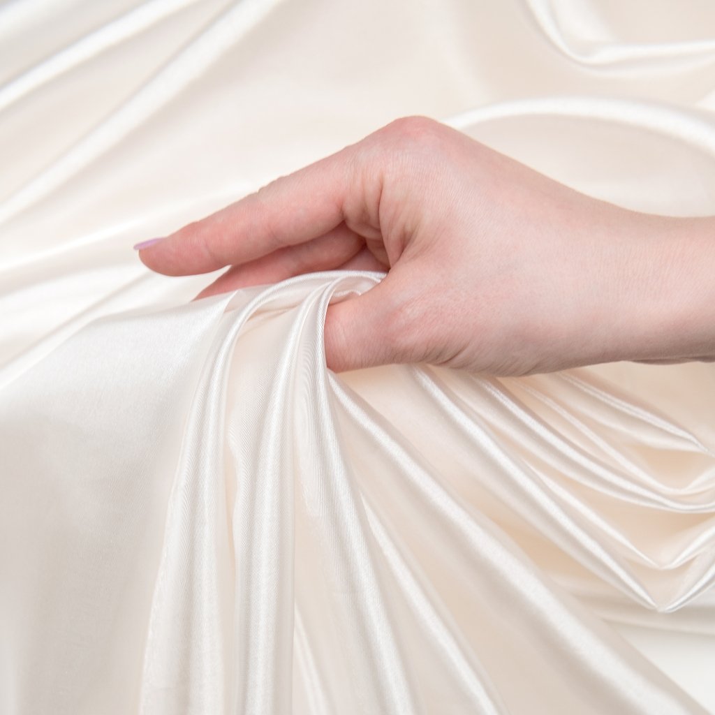 A close-up of a hand gently gathering luxurious white organza fabric, highlighting its smooth, sheer, and lustrous surface.