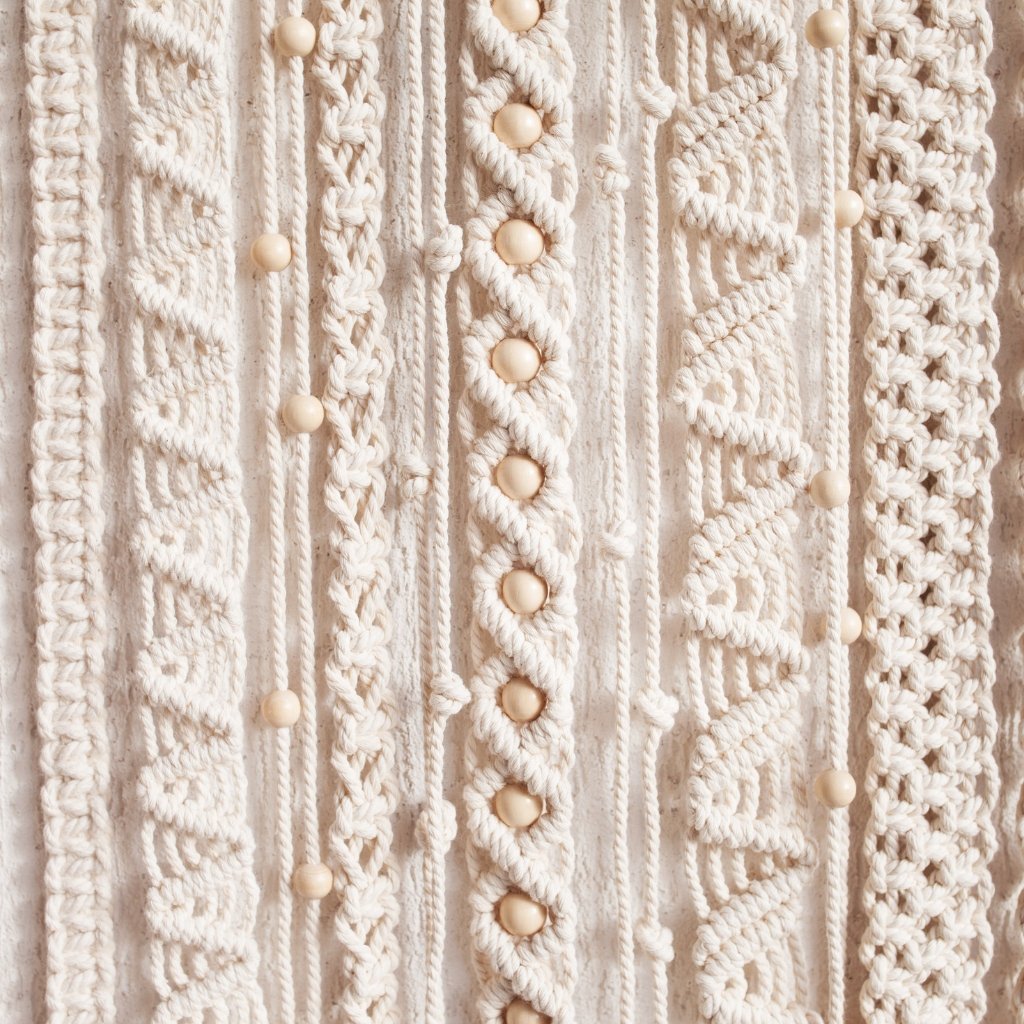Why Supima Cotton Feels Softer, Stronger, and Smarter 14 A close-up view of intricate macramé-style woven fabric in soft, natural cream tones. The textile features multiple cords and patterns with small, rounded cream buttons or beads interspersed throughout, highlighting texture and craftsmanship. why supima cotton
