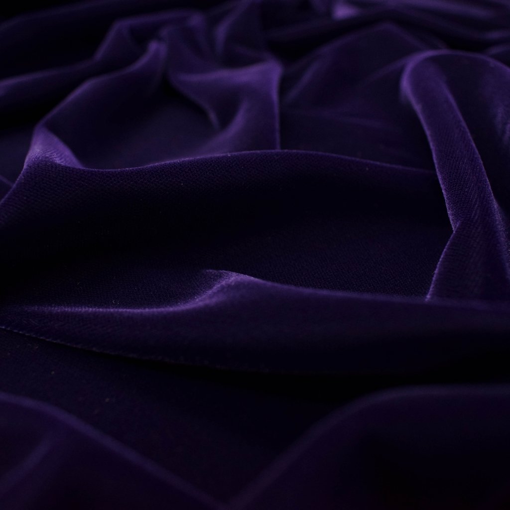 Close-up of luxurious purple corduroy wool fabric with soft folds and subtle texture.