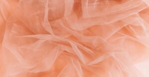 Soft peach-colored crushed organza fabric with irregular folds and sheer texture.