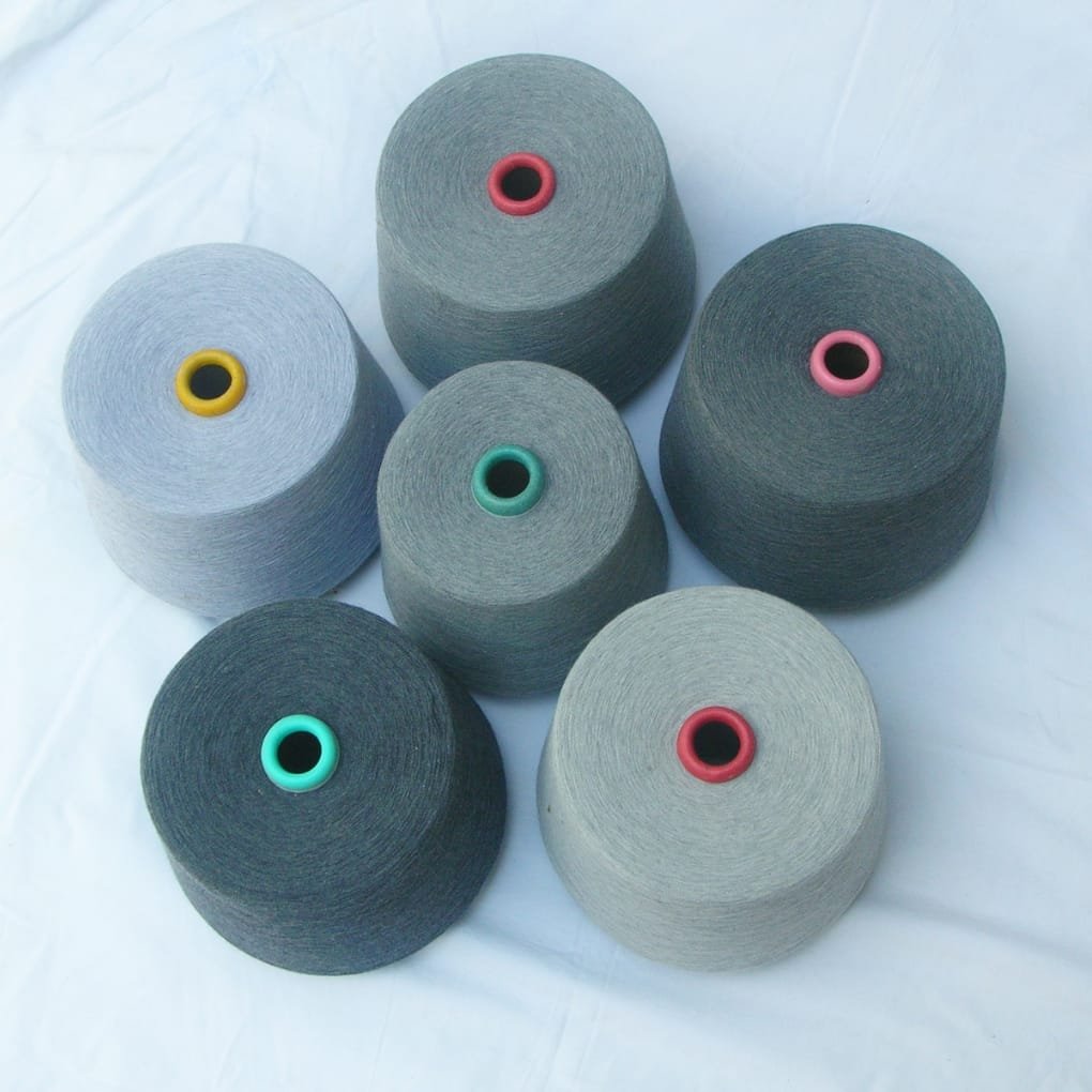 A collection of colored yarn cones in varying shades of gray and blue arranged on a light surface, each with a bright plastic core in colors like green, yellow, red, and pink.