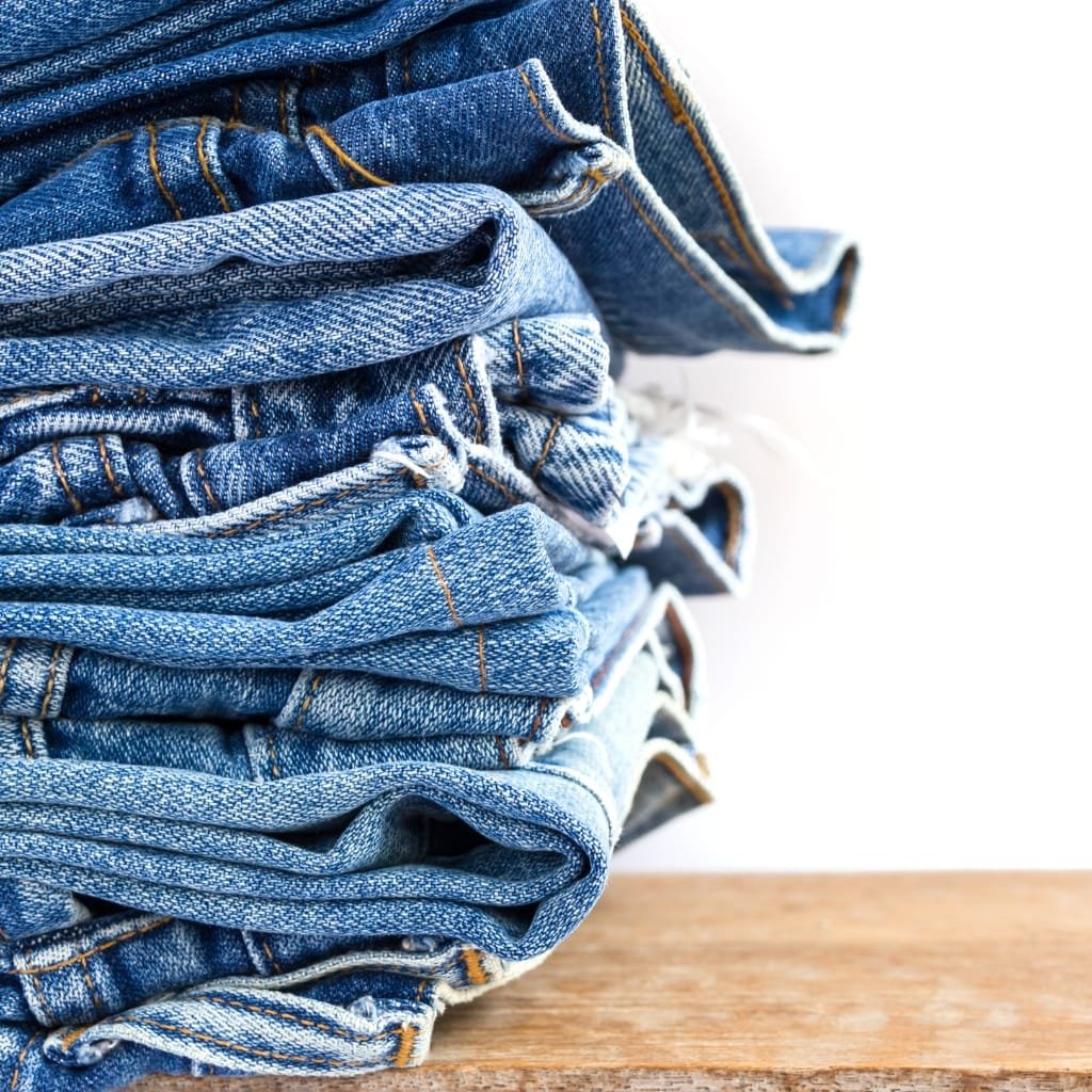 Stack of folded blue denim jeans with visible orange stitching resting on a wooden surface.