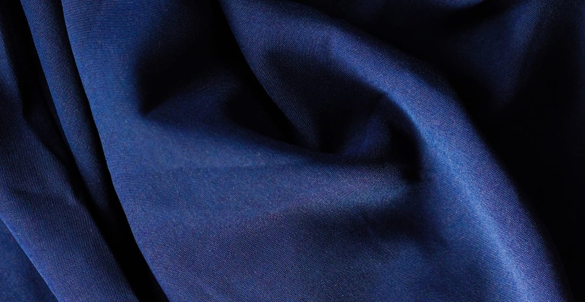 Drill Cotton Fabric: What It Is & How to Use It A close-up shot of smooth, deep blue fabric with soft folds and shadows.