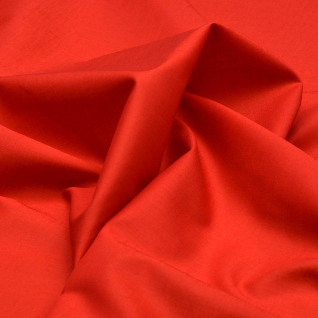 A close-up of bright red fabric with soft folds and shadows. batiste cotton fabric