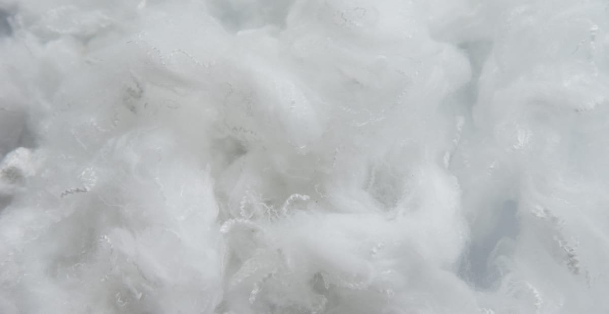 A close-up view of fluffy, white hollow polyester fiber clusters, resembling soft cloud-like material.
