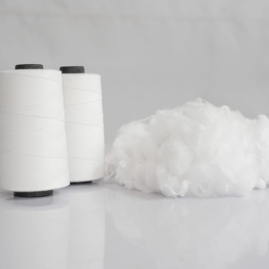Two white spools of hollow polyester fiber (thread spools) standing upright next to a fluffy white fiber tuft on a glossy surface.