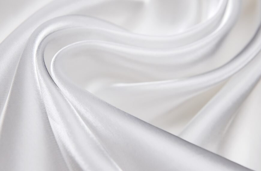 Close-up of smooth, white organza fabric softly draped and folded, showing delicate sheen and light creases.