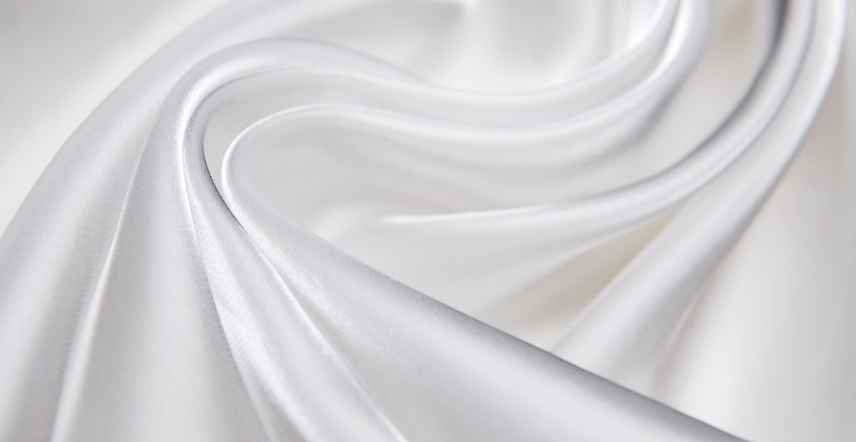 Close-up of smooth, white organza fabric softly draped and folded, showing delicate sheen and light creases.