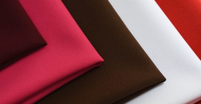 Several folded fabric swatches in a stack, featuring pink, magenta, brown, white, and red colors.
