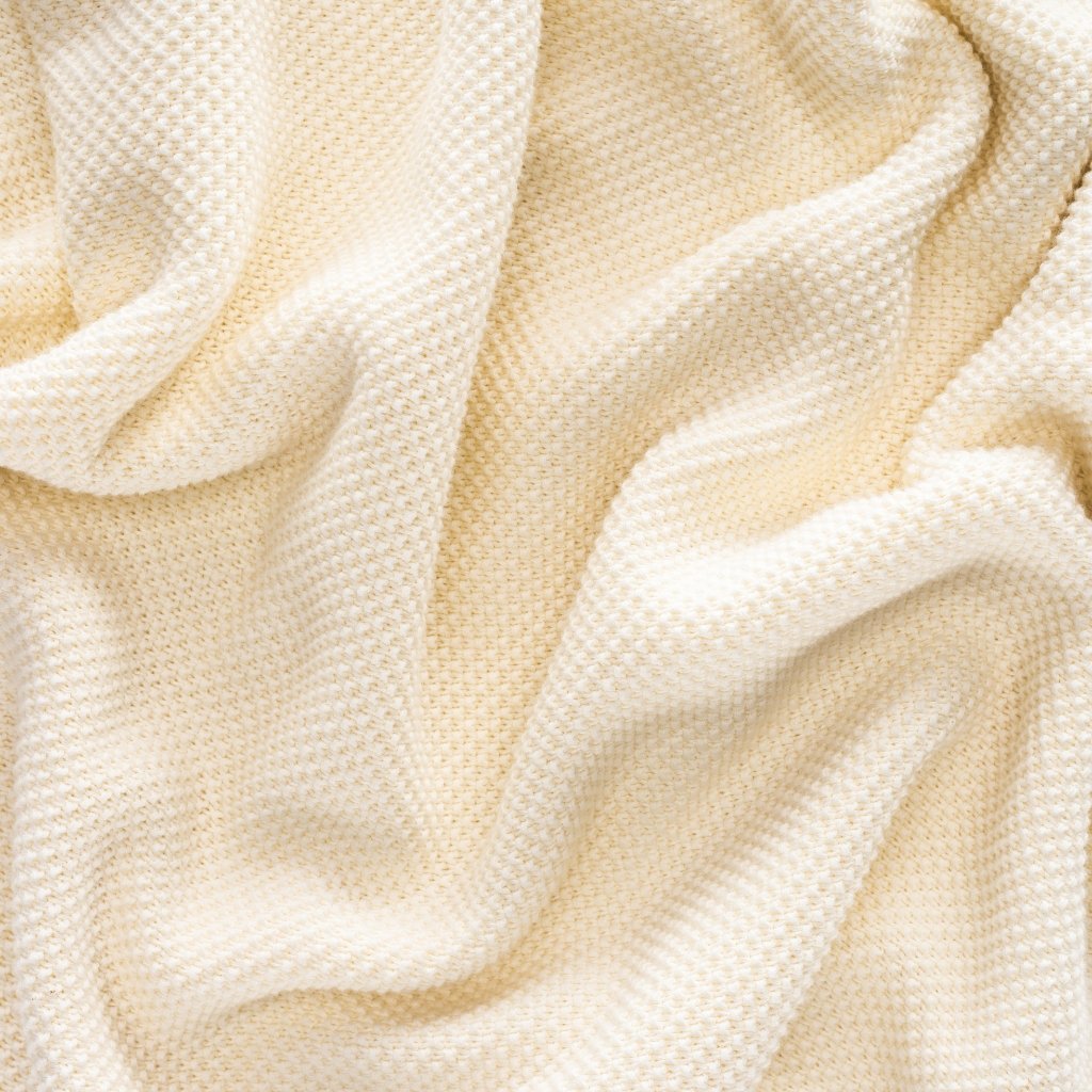 A close-up view of soft, cream-beige fabric with a textured waffle-knit pattern, draped in gentle folds.