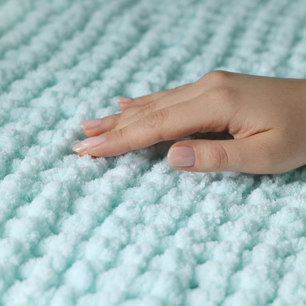 A close-up of a hand with light skin and neatly manicured nails resting palm-down on a fluffy, light aqua-blue textured surface. what is interlock cotton