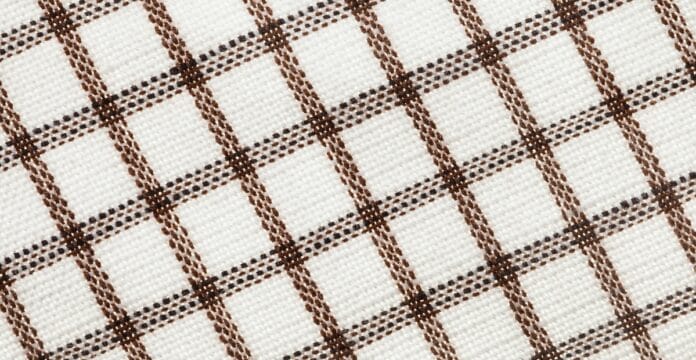 Close-up view of a white fabric with a brown checkered plaid pattern, showing intersecting thin and thick brown lines on a textured weave.