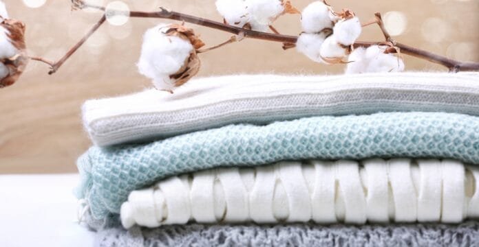 Stacked folded fabrics in soft pastel tones with cotton bolls on a branch above.