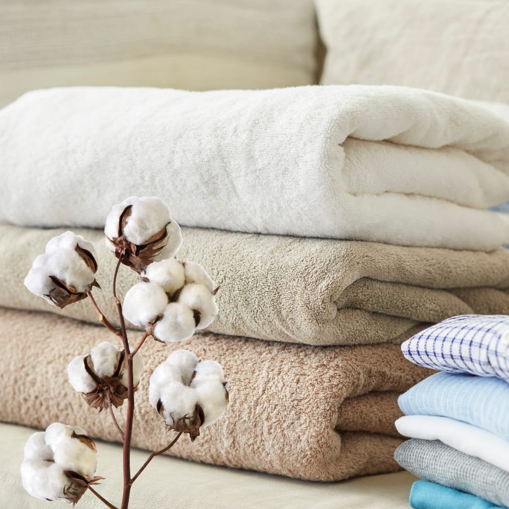 Stack of folded towels in white, beige, and pastel colors with a cotton plant branch in the foreground.