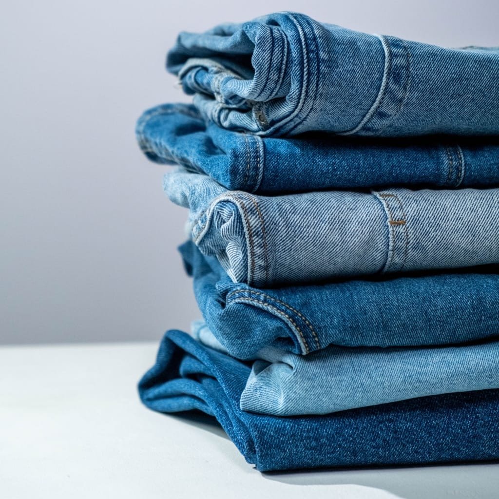 A neatly stacked pile of folded blue jeans in varying denim shades on a light surface.