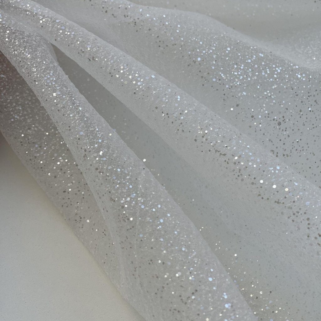 Close-up of sheer white fabric with silver glitter specks scattered across the surface, draped in soft folds.