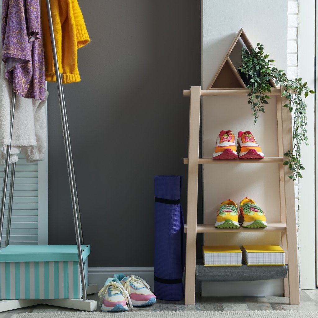 Indoor retail or display area with a wooden shelf showcasing colorful sneakers, a purple yoga mat, a blue striped storage box, and potted greenery; clothing on a rack to the left.