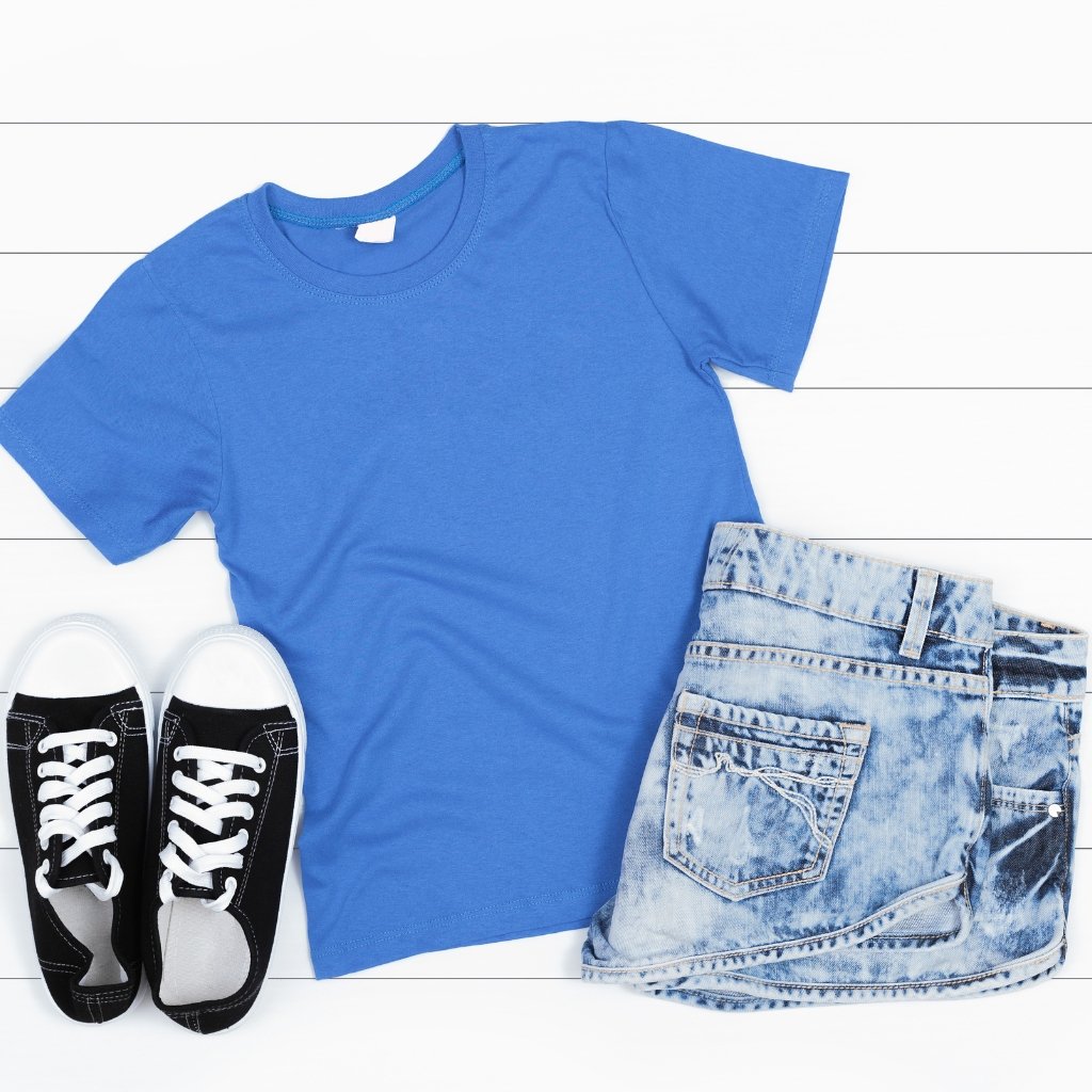 Flat lay of a blue T-shirt, distressed light-wash denim shorts, and black-and-white sneakers arranged on a white wooden surface; no visible sherpa wool fabric shown.