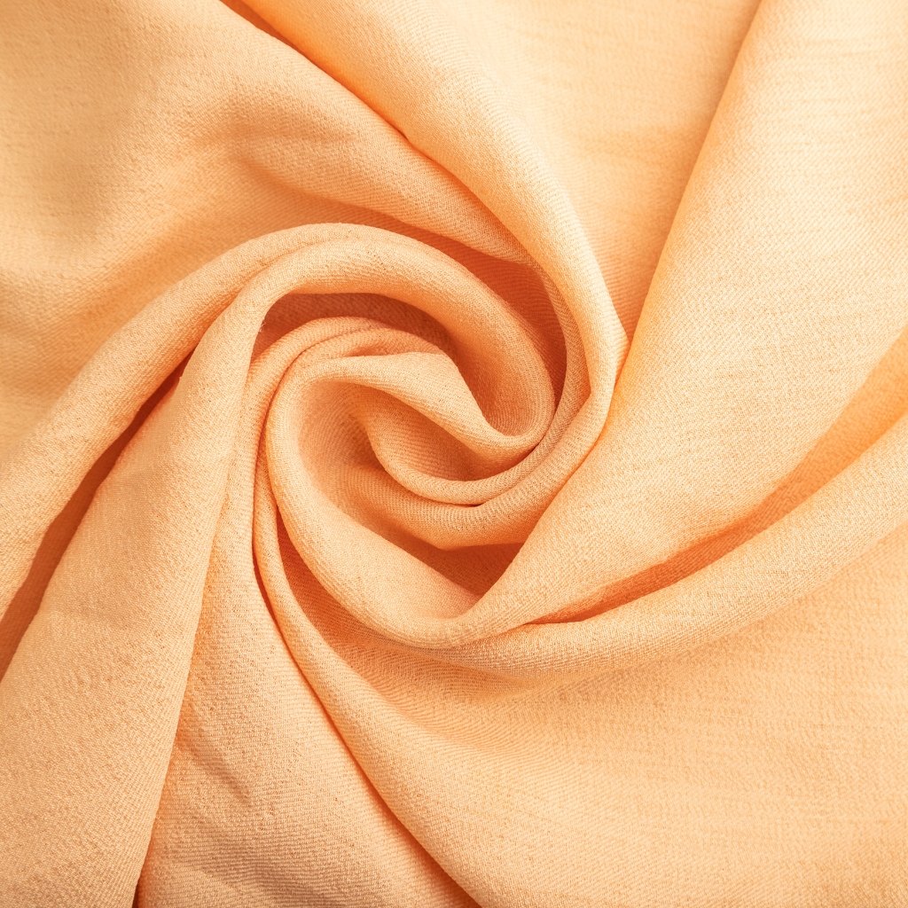 Soft peach fabric folded into a gentle swirl, showing smooth texture and warm peach color.