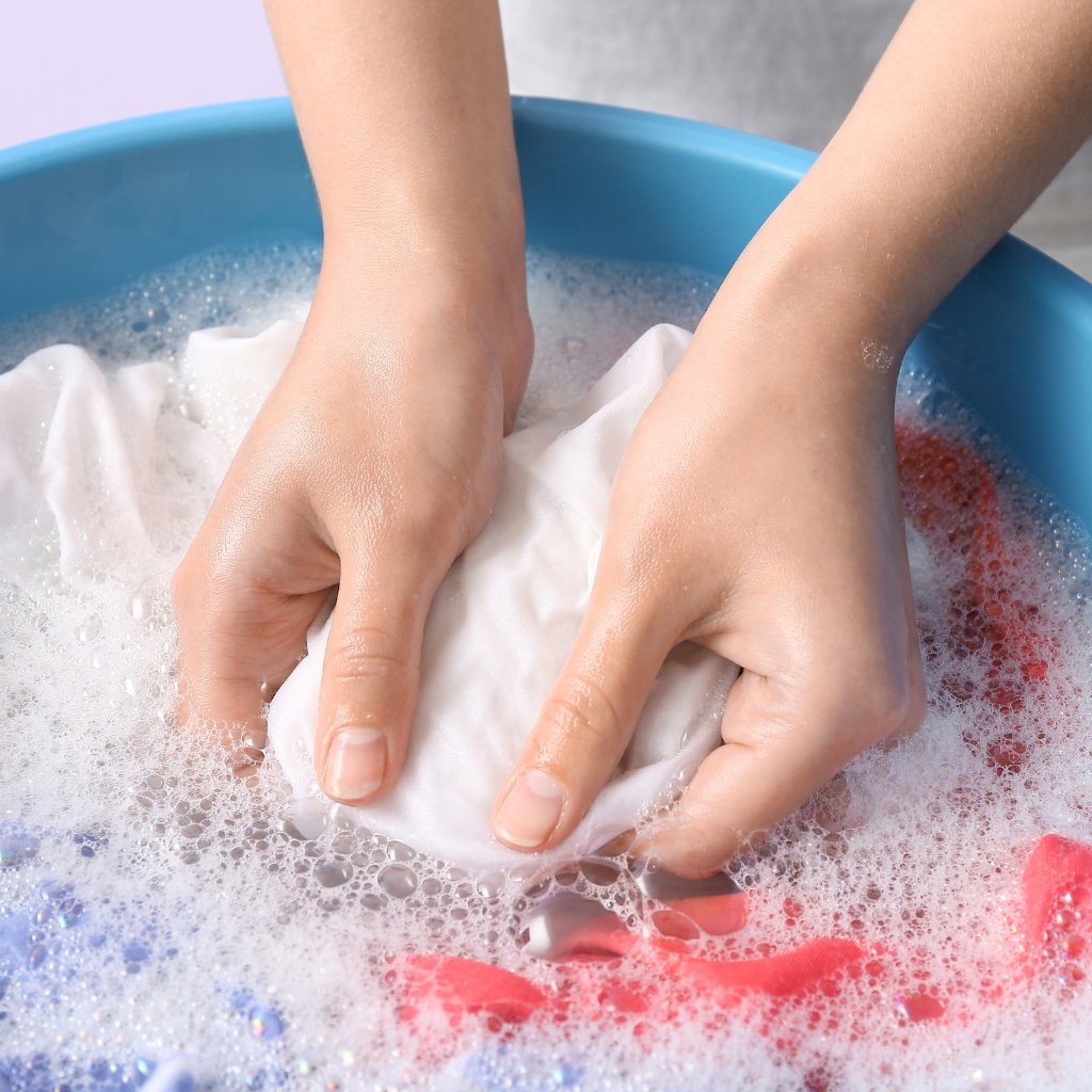 Black Organza Fabric: A Timeless Choice for Stylish Outfits 16 A pair of hands wringing a white cloth in soapy water inside a blue basin, with colorful fabrics and bubbles.