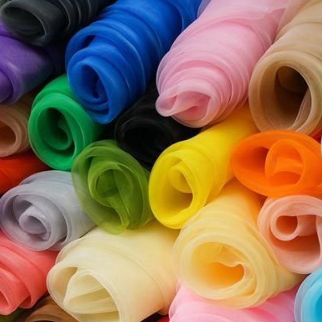 Stack of rolled satin organza fabrics in assorted colors including blue, pink, green, yellow, orange, purple, lavender, beige, black, gray, and red