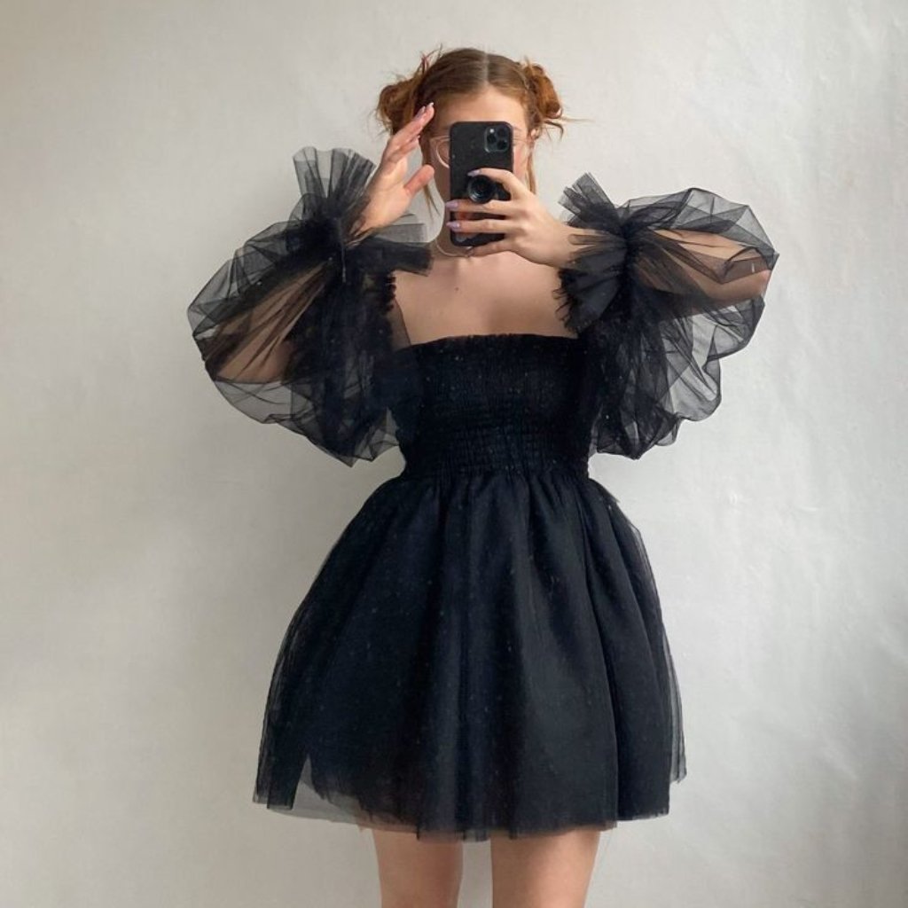 Black Organza Fabric: A Timeless Choice for Stylish Outfits 13 A person wearing a black off-the-shoulder dress with voluminous sheer tulle sleeves, taking a mirror selfie with a smartphone.