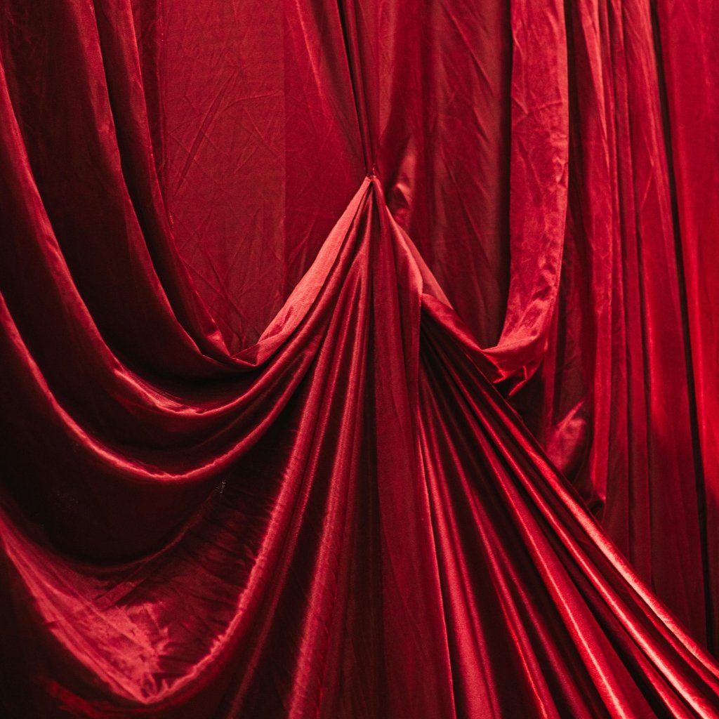 Deep red velvet curtains gathered into a central knot with folds cascading downward.