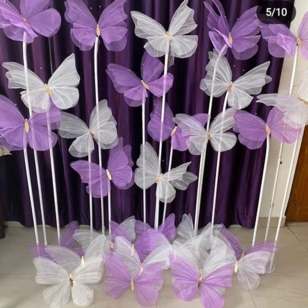 "Display of tall white poles with large translucent purple and white butterfly decorations arranged in front of a dark purple curtain.