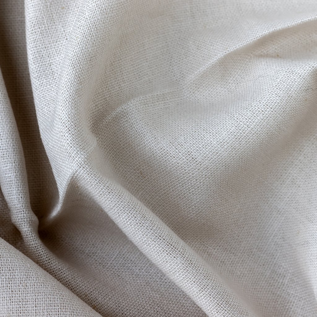 A close-up of light, beige-white fabric with visible woven texture and soft folds.