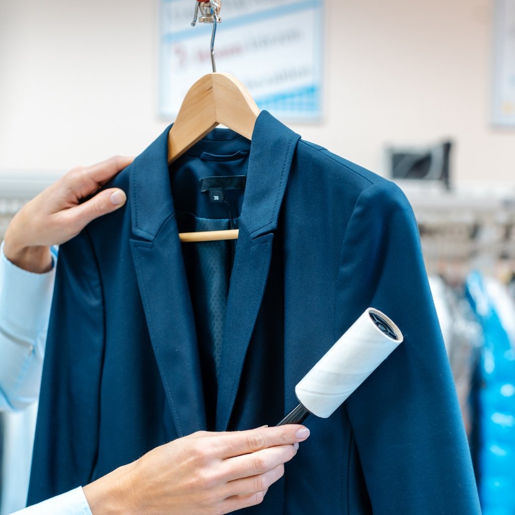 A person is ironing a navy blue blazer on a hanger in a clothing store.
