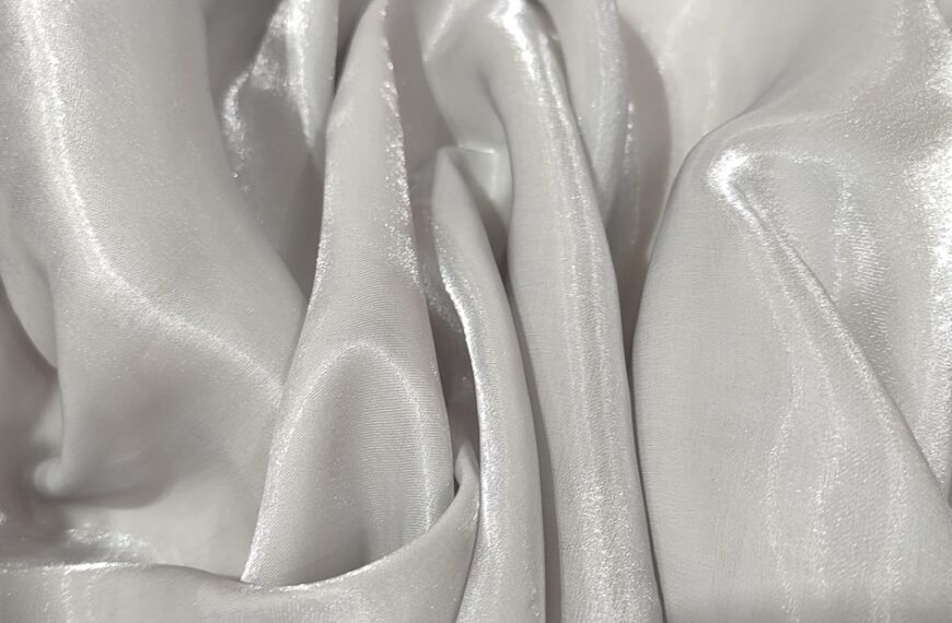 Close-up of lustrous metallic organza fabric with soft, flowing folds and a subtle sheen that reflects light. Metallic Organza Fabric