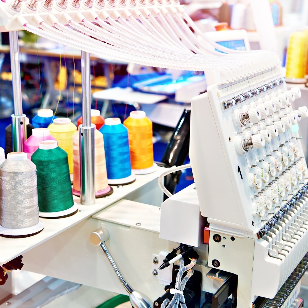 Industrial embroidery/overlock sewing machine with multiple spools of chenille wool threads in bright colors (silver, green, pink, yellow, blue, orange) on a quilting or embroidery setup.
