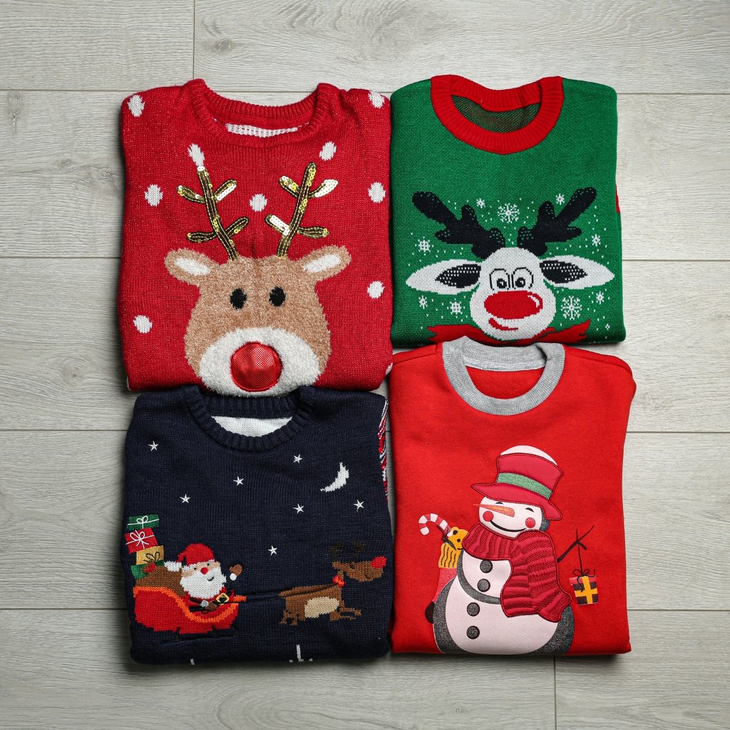 Sheep Wool Clothing: Natural Warmth and Timeless Style 16 Four folded Christmas sweaters with holiday designs (reindeer, reindeer face on green, Santa with sleigh, and snowman) arranged on a light wooden floor.