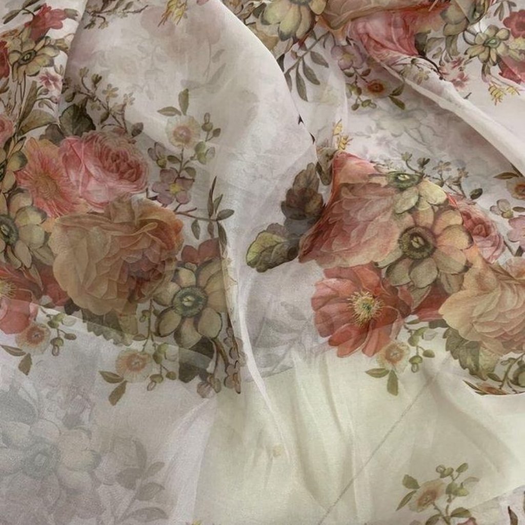 A sheer floral-patterned fabric with large pink and peach roses and green leaves, draped and slightly translucent over a light background.