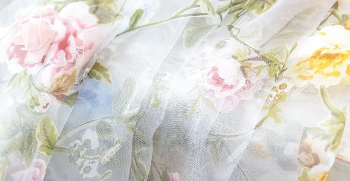 Flower Organza Fabric Ideas to Elevate Fashion and Interiors translucent floral fabric with pastel pink, yellow, and green flowers and leaves. The sheer material creates delicate folds and a light, airy look. Flower Organza Fabric