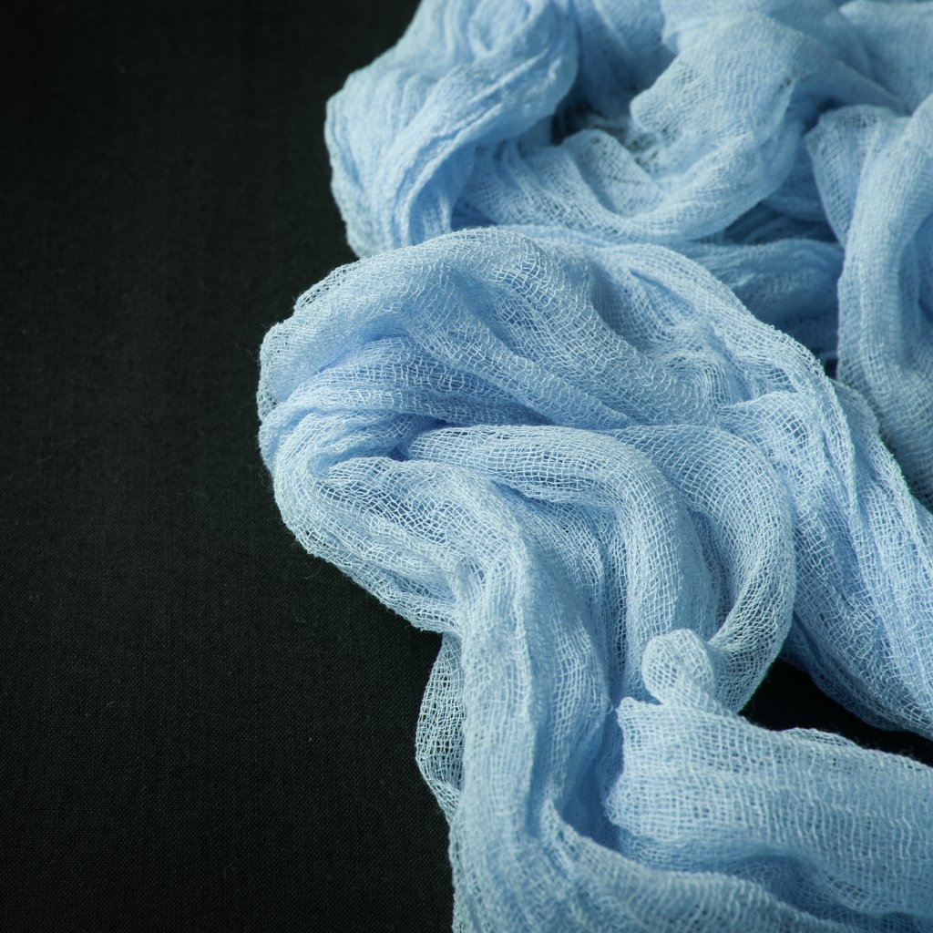 Light-blue gauze fabric loosely gathered on a dark surface, showing a sheer, mesh-like texture with soft folds.