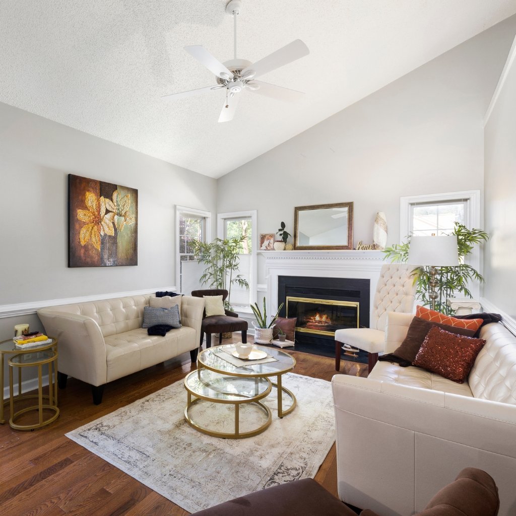 Bright living room with a light gray wall, white fireplace, cream suede wool sofa and chair, glass coffee table with gold frame, and a large abstract floral painting on the wall.