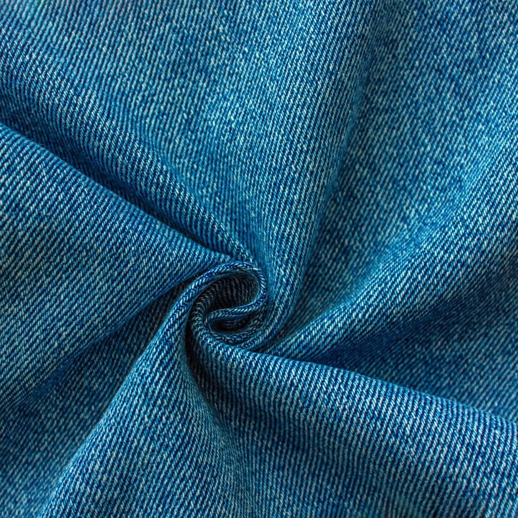 “Close-up view of blue rayon denim fabric, showing diagonal twill weave and folded swirl with subtle color variations.”
