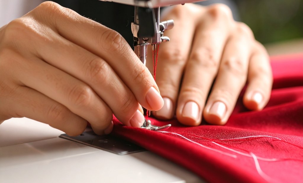 Close-up of hands guiding a sewing machine as clear red organza fabric is stitched; the needle, presser foot, and thread are visible, indicating a sewing session. How to Sew Organza Fabric